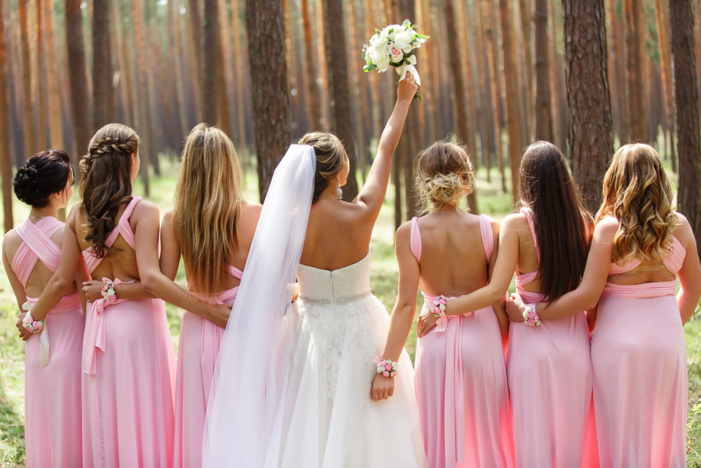 Line of bridesmaids in pink bridesmaid dresses with bride in the middle holding up her bouquet