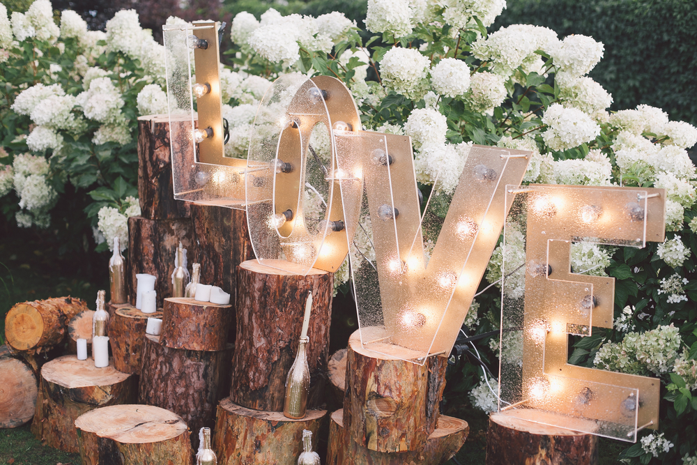 Light up Love Sign on tree stumps with white flowers in background